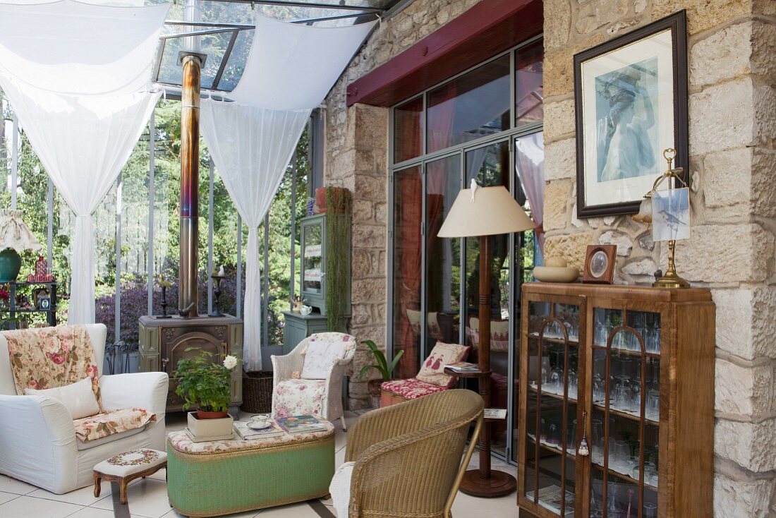 Antique furniture, wicker chairs in seating area and crystal glasses in olf display cabinet in vintage-style conservatory