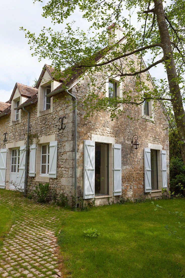 Rustikales Landhaus aus Naturstein mit weissen Fensterläden und Fenstern in sommerlichem Garten