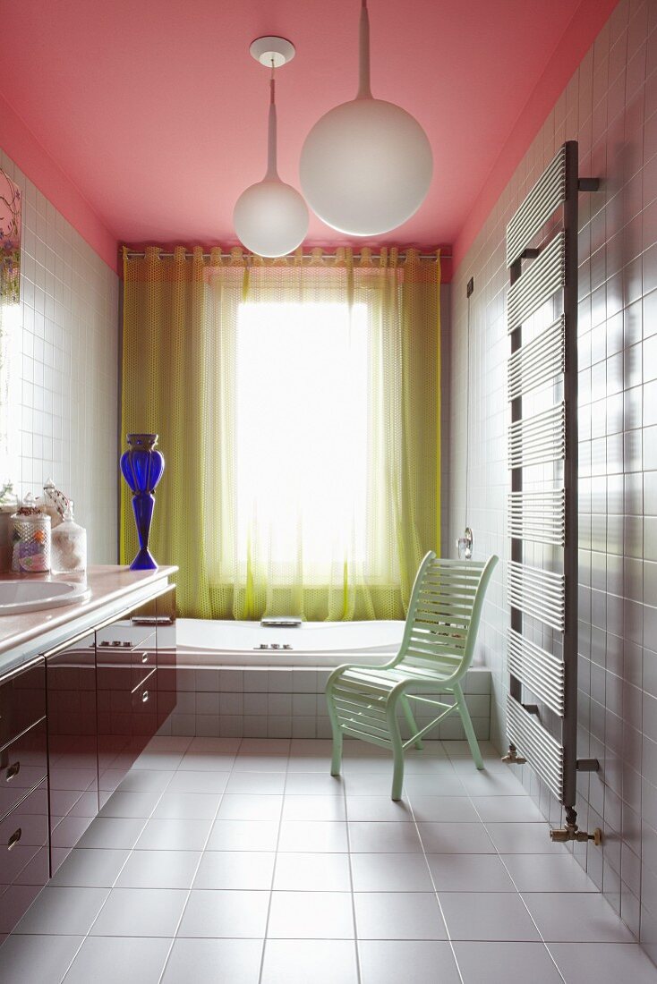 Colourful modern bathroom with pink ceiling, yellow perforated curtain, mint green chair and blue glass vase