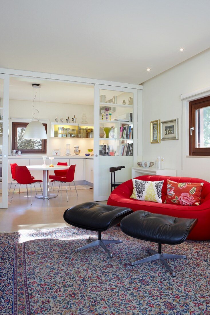 Glass sliding doors between dining area and living area; red designer couch and black leather footstools