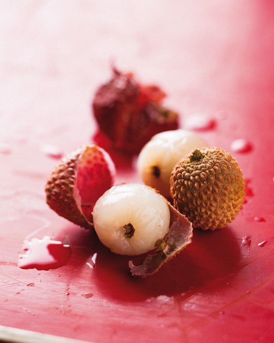 Peeled and unpeeled lychees on a red surface (close-up)