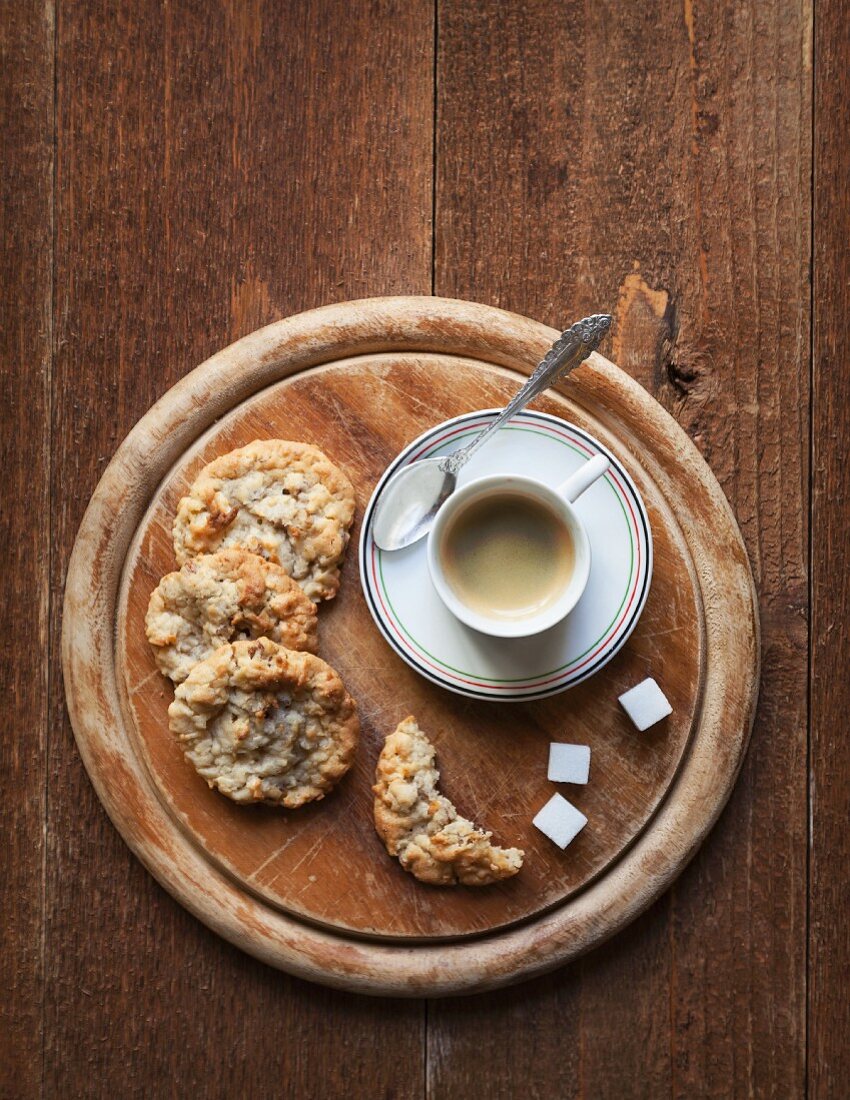 Eine Tasse Espresso mit Cookies auf rundem Holzbrett (Aufsicht)