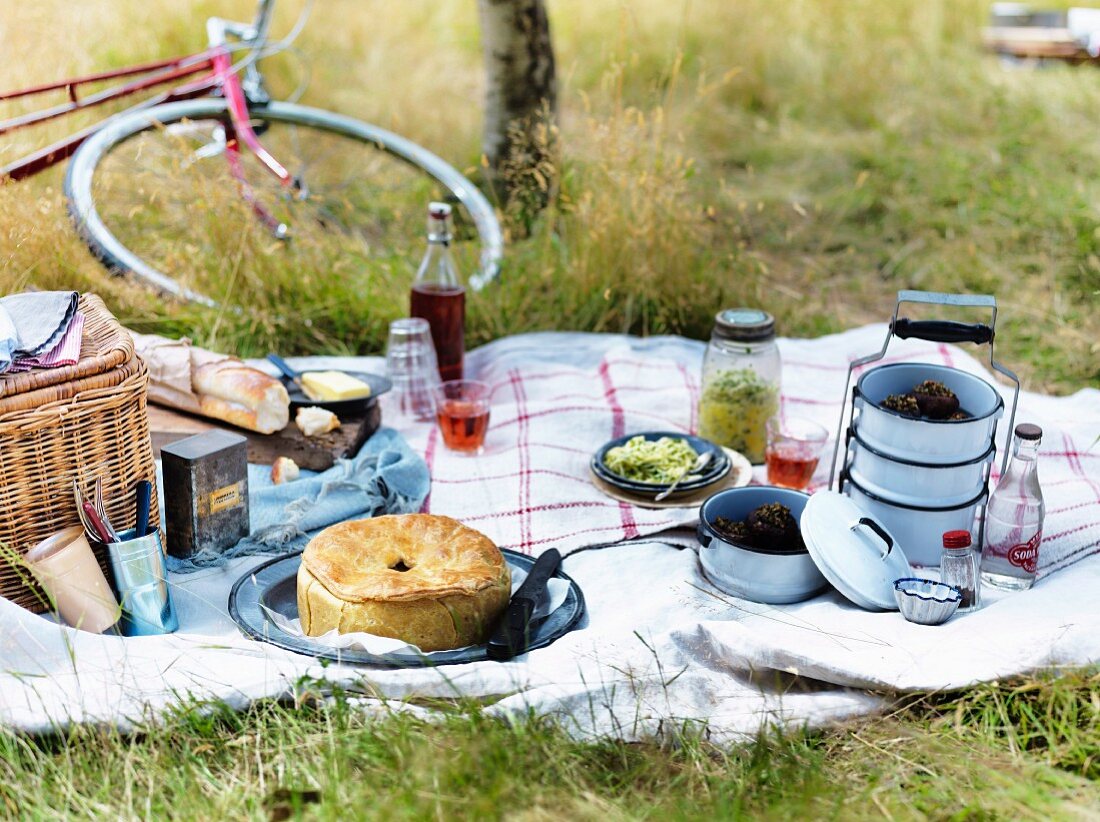 Picnic with various dishes on white tablecloth, a bicycle in the background