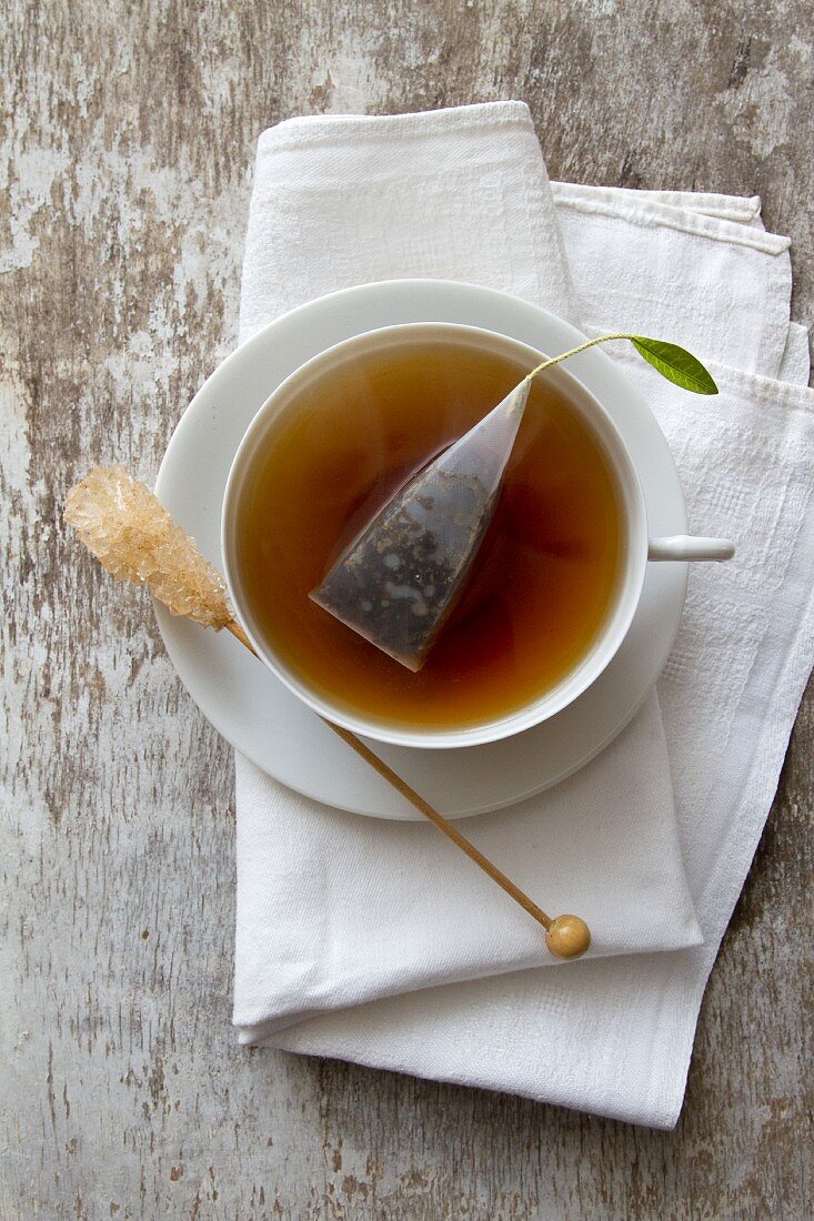 A cup of tea with a tea bag and rock candy stick on a saucer