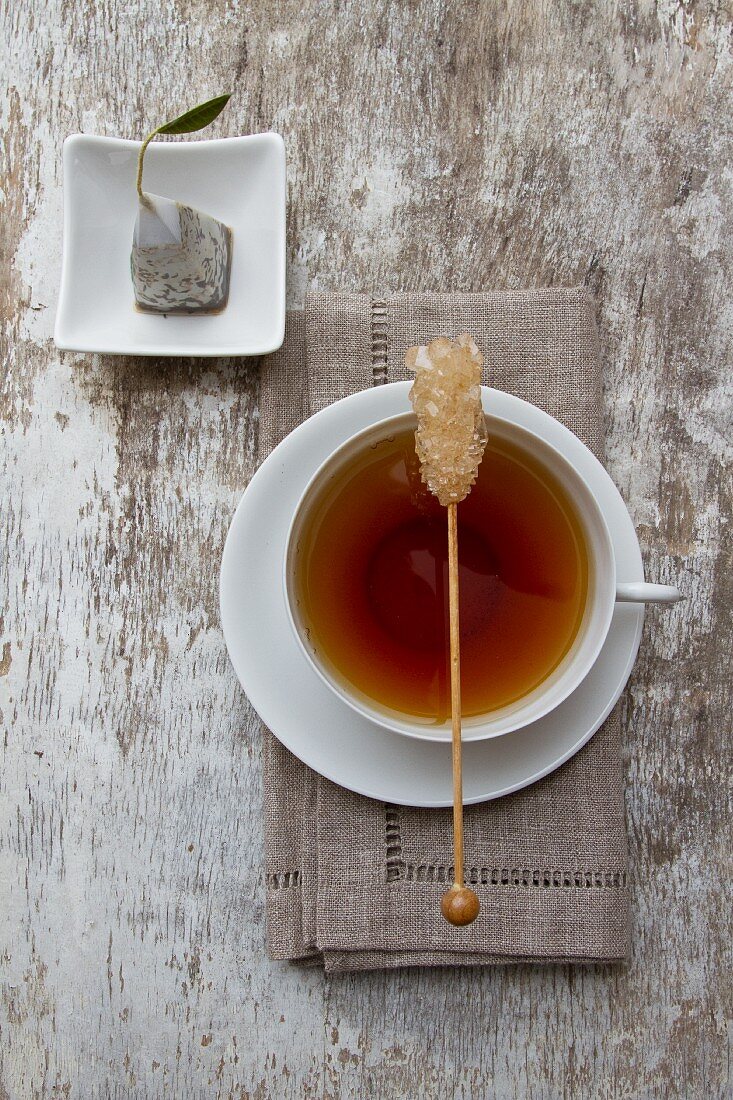 A cup of tea with a stick of rock sugar with a tea bag next to it