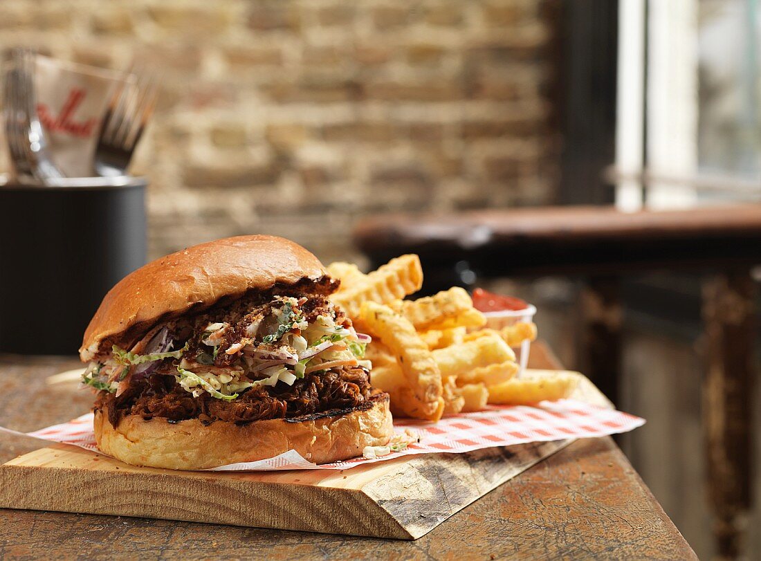 A pulled pork burger and chips on a rustic wooden board