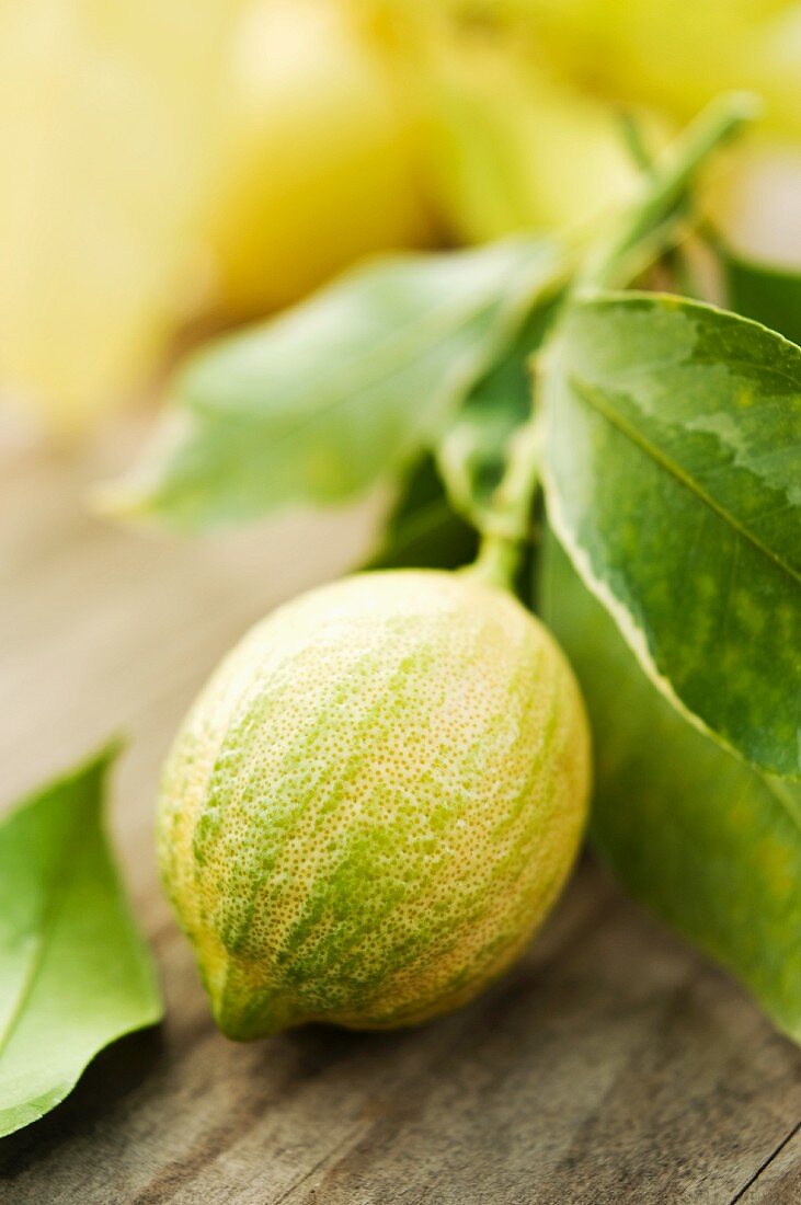 A lemon with a stem and leaves on a wooden surface