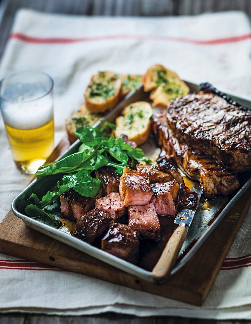 Grilled marinated beef steaks with garlic bread, salad and beer
