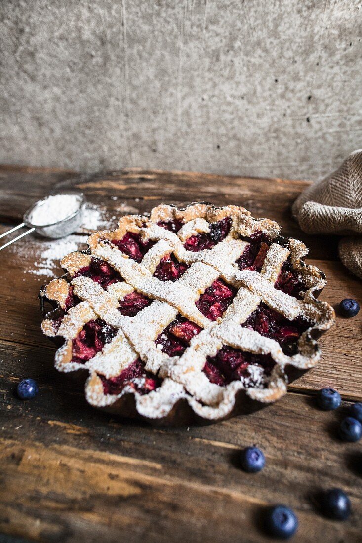 A blueberry tart with a lattice lid and icing sugar