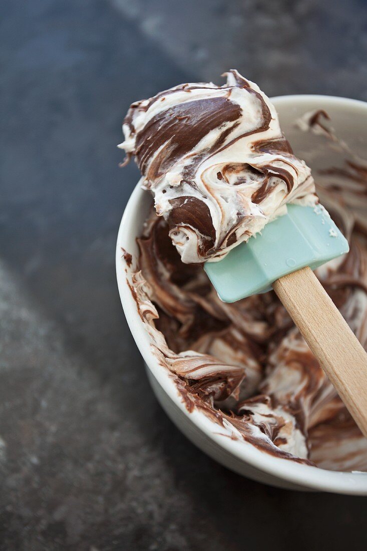Chocolate and vanilla frosting being stirred in a mixing bowl