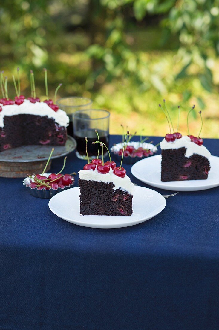 Schokoladenkuchen mit Frischkäseglasur und frischen Kirschen auf Gartentisch