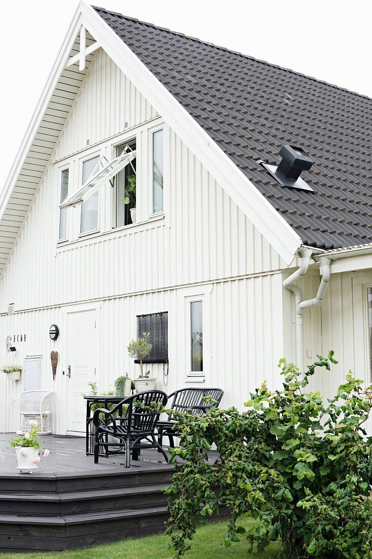 Wohnhaus mit weiss gestrichener Holzfassade, Outdoor-Möbel auf erhöhter Holzterrasse