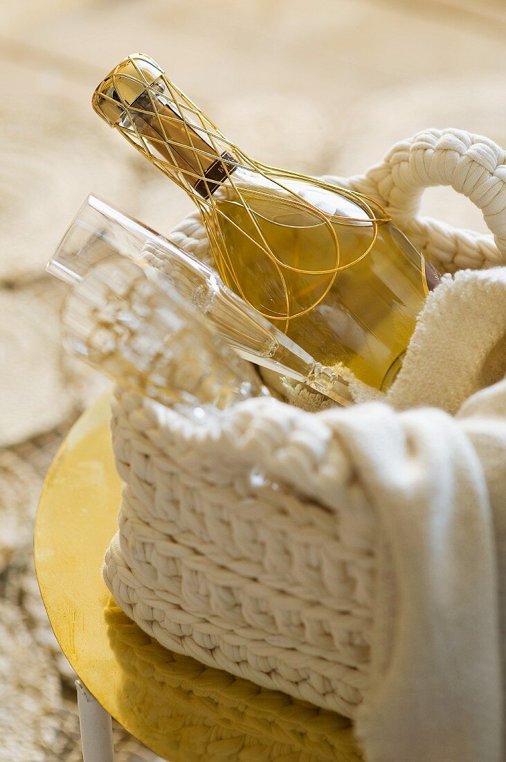 A bottle of champagne with two glasses in a crocheted basket