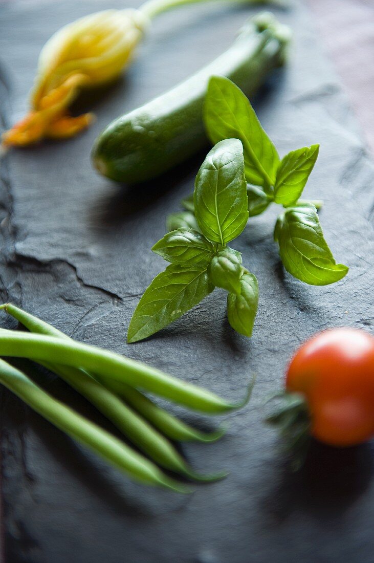 An arrangement of fresh vegetables and basil on a slate surface