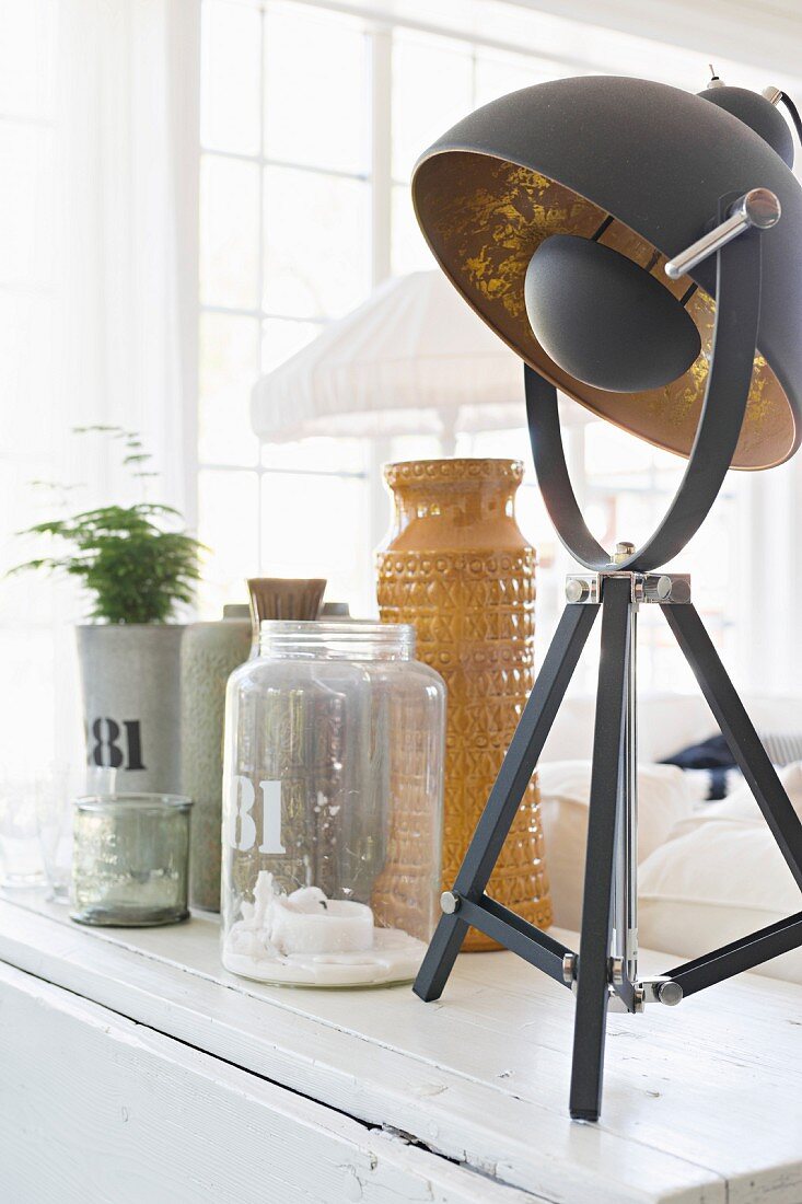 Table lamp with black and gilt lampshade next to vintage glass and ceramic vessels