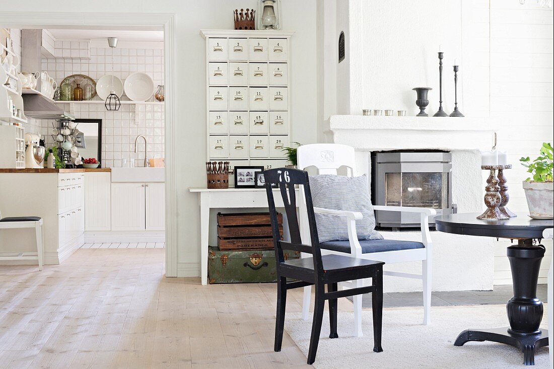 Round black table and chairs in front of fireplace next to wide, open doorway with view into kitchen