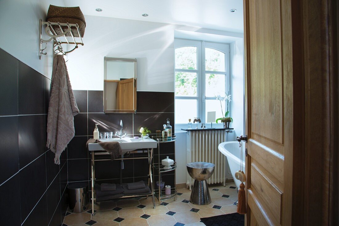 Washstand against wall with black-tiled dado and white lattice window in renovated country-house bathroom