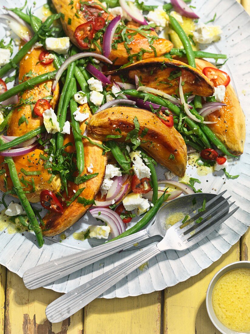 A salad with roasted sweet potatoes, green beans, feta cheese and red onions