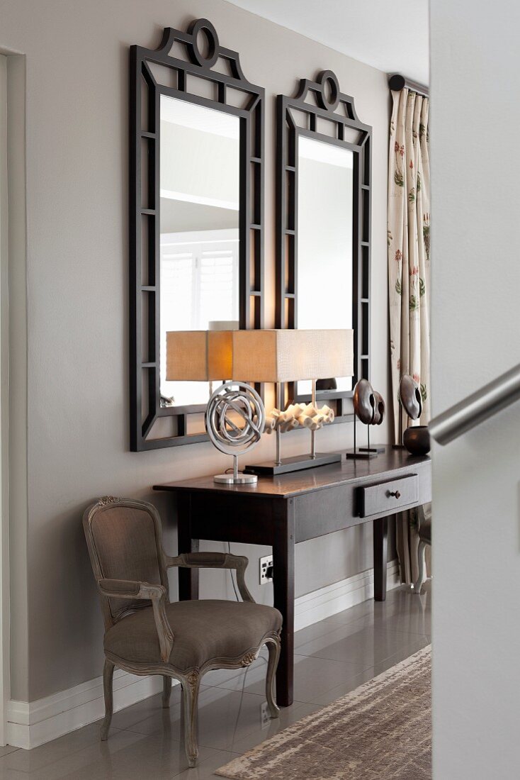 Dark console table next to Baroque armchair below two black-framed mirrors in elegant hallway