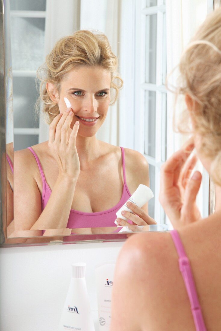A blonde woman applying face cream