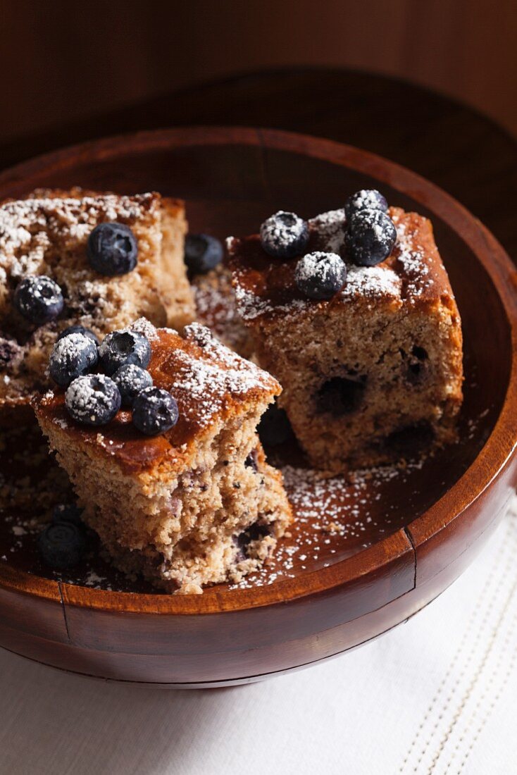 Drei Stücke Heidelbeer-Streusel-Kuchen in einer Holzschale mit Puderzucker