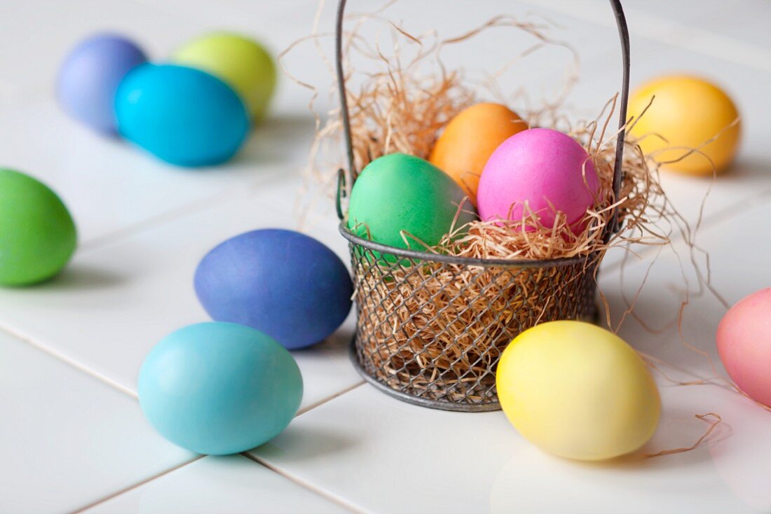 Colourful Easter eggs in and next to a wire basket lined with straw
