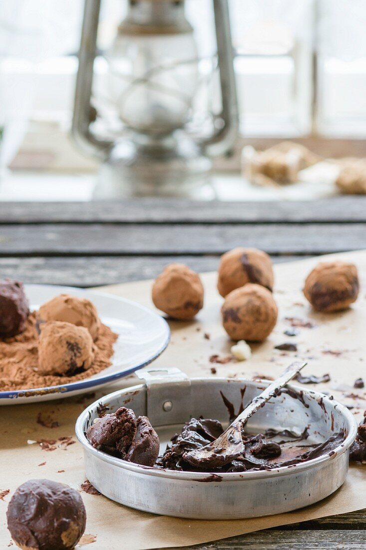 Homemade chocolate truffles with ingredients on an old wooden table in front of a window