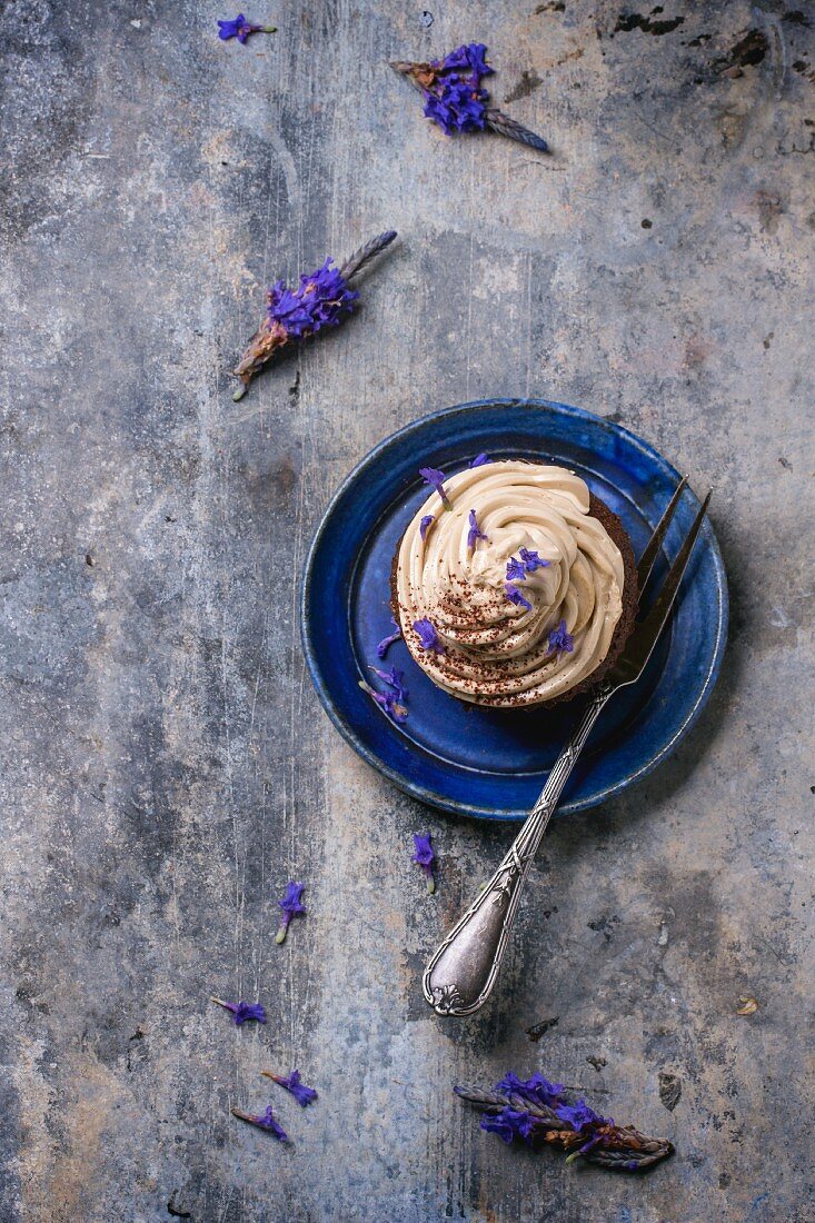 Schokoladencupcake mit Kaffee-Buttercreme und Lavendelblüten auf blauem Teller