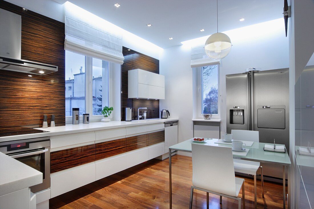 Dining area with breakfast place settings in designer kitchen with white and wooden surfaces and indirect lighting on ceiling