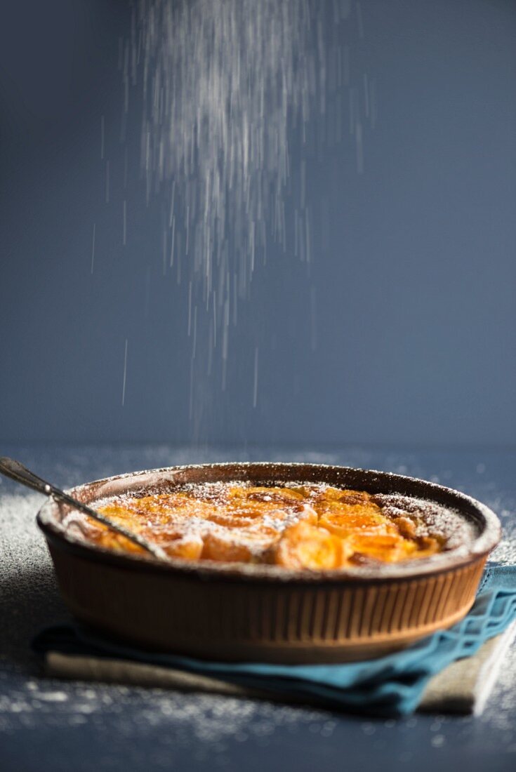 Apricot clafoutis being dusted with icing sugar