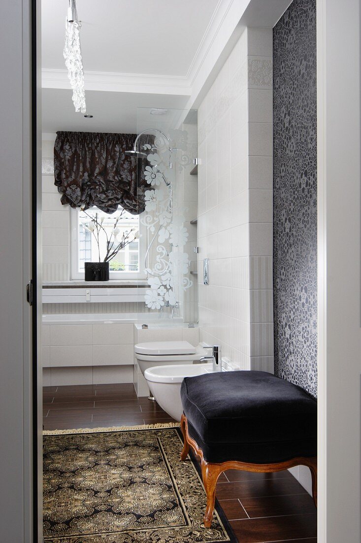 Antique ottoman with black velvet cover and rug on tiled floor in comfortable bathroom with modern ambiance