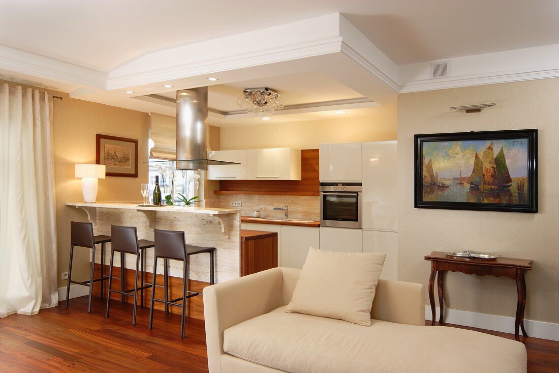 Pale, classic-style chaise longue in front of modern kitchen area with bar stools at counter in traditional interior