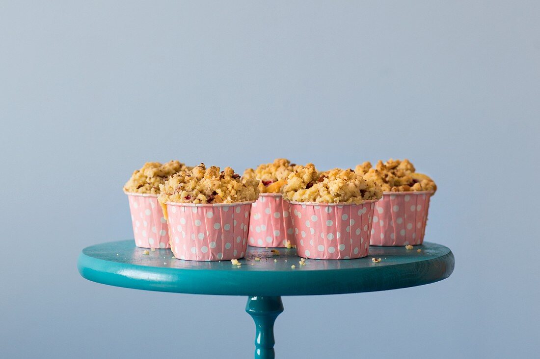 Himbeer-Streusel-Muffins in rosa gepunkteten Förmchen auf blauem Kuchenständer