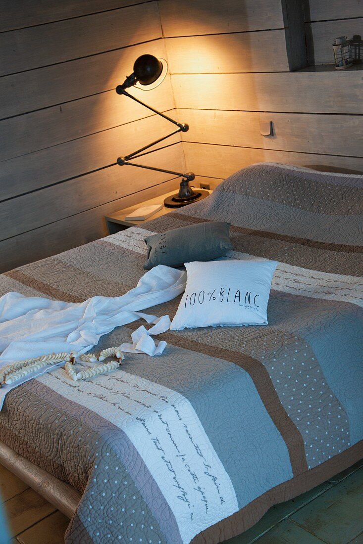 Double bed with grey and brown striped bedspread and illuminated retro table lamp on bedside table