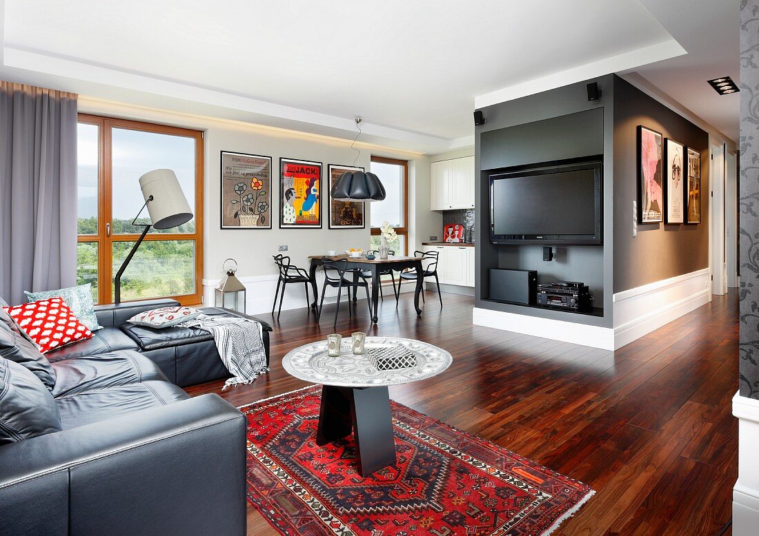 Leather sofa, side table on Oriental rug and flatscreen TV in open-plan lounge area with exotic-wood parquet floor