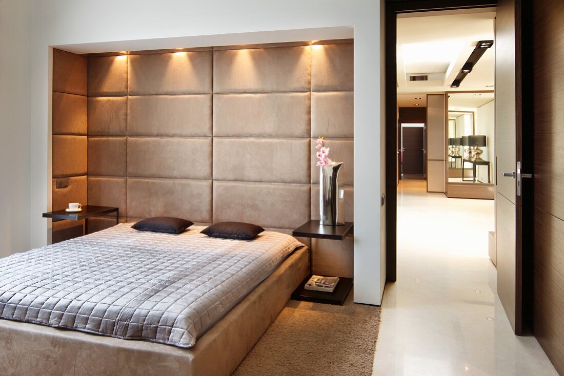 Bedroom in austere, classic style with French bed in upholstered niche with ceiling spotlights; open door leading into corridor