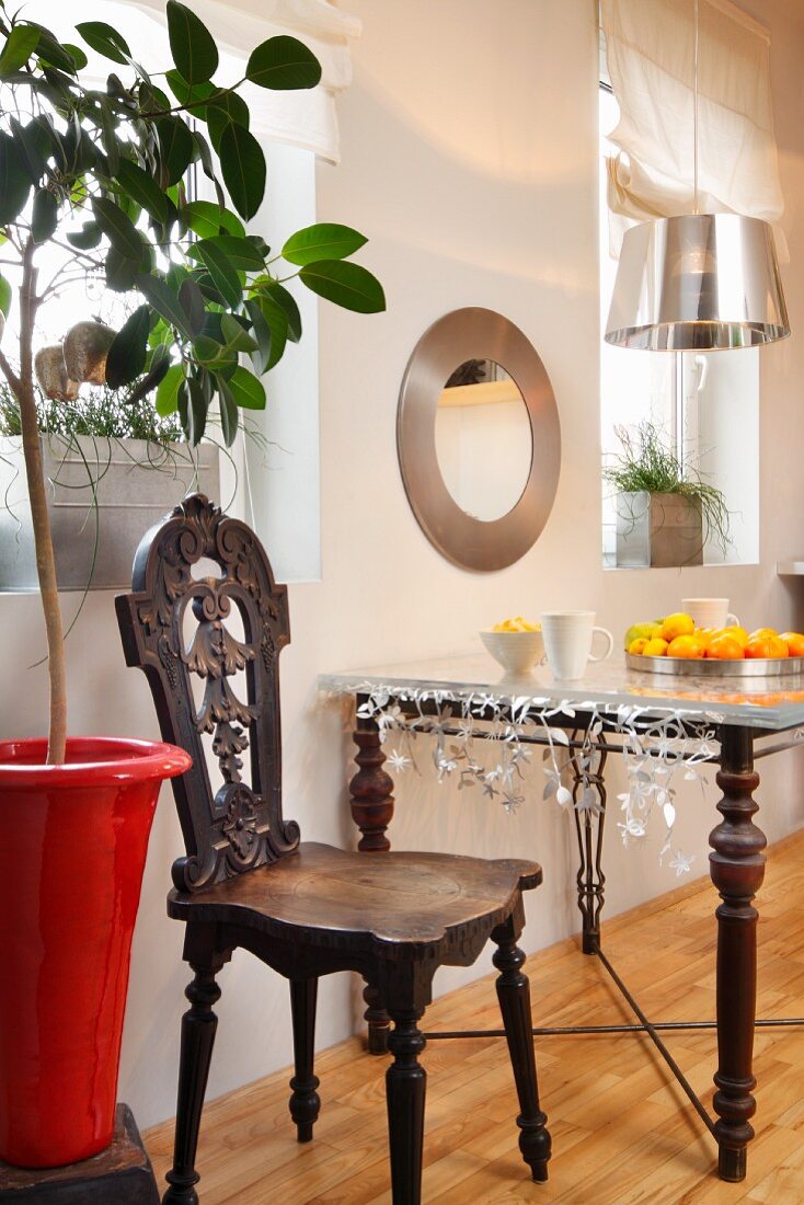 Bulls-eye mirror above table constructed from turned wooden legs, metal stretchers and glass top next to antique chair in youthful kitchen