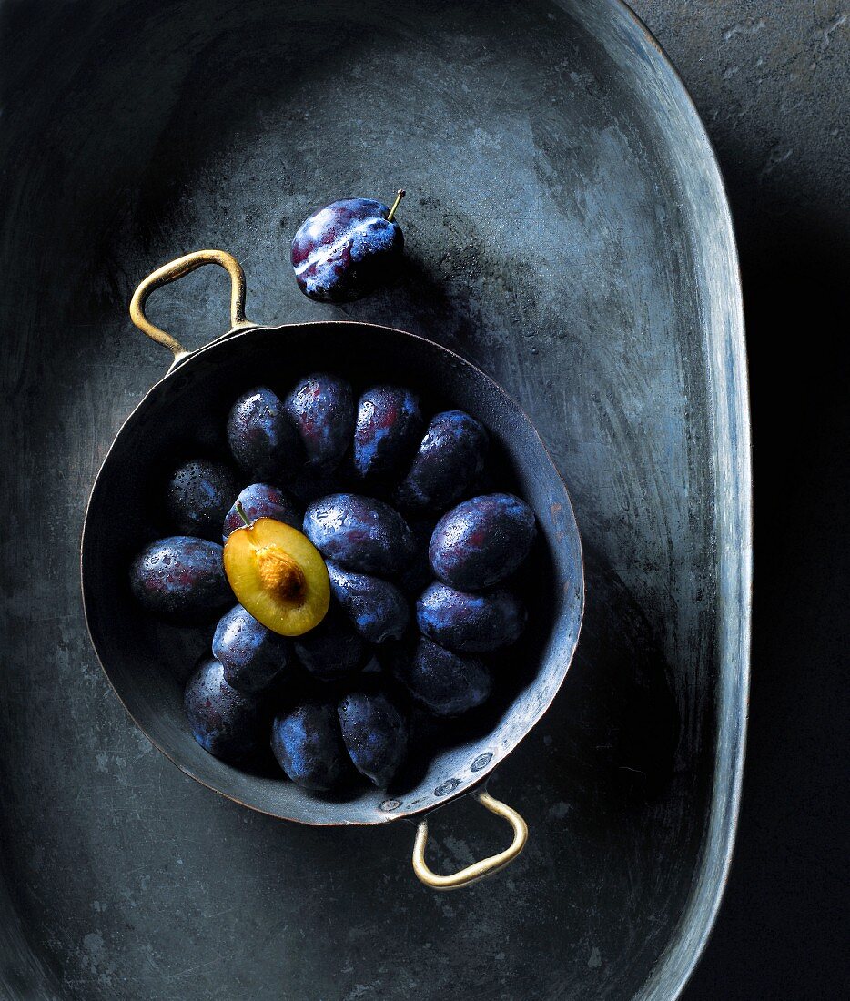 Fresh plums in a metal bowl (seen from above)