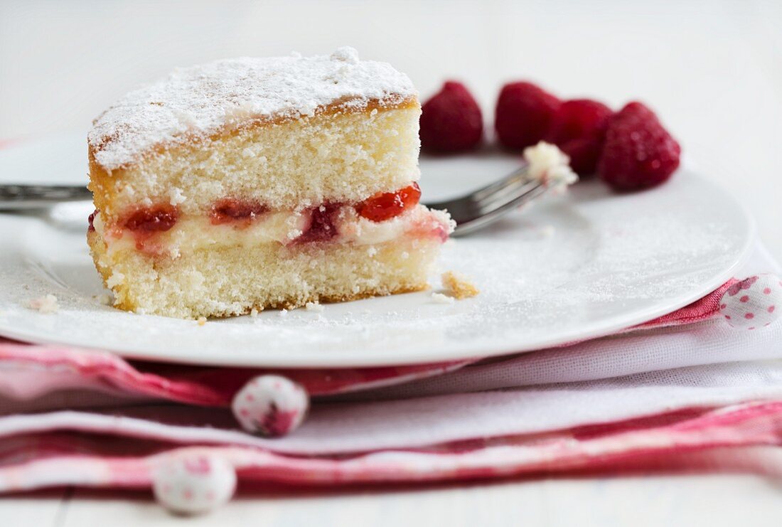 A slice of Victoria sandwich cake with raspberries