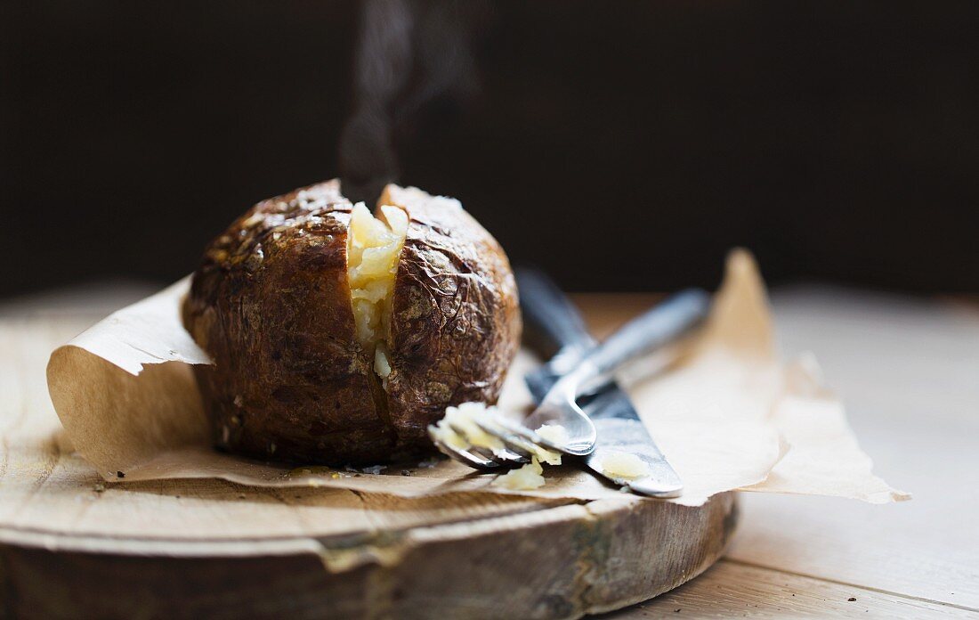 A steaming baked potato on a piece of baking paper