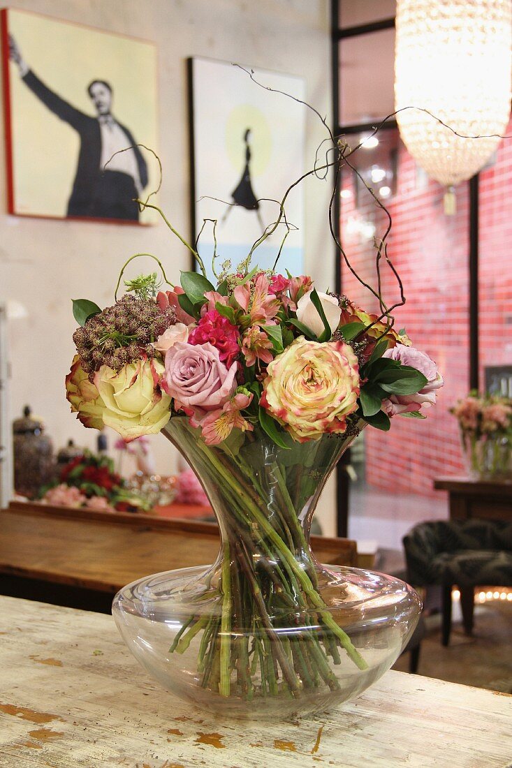 Bouquet with willow twigs in glass vase on vintage wooden surface