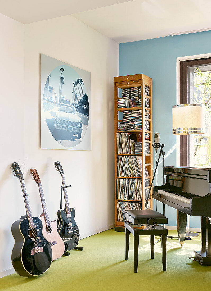 Various musical instruments in front of narrow, tall wooden shelved in corner of room against wall painted pale blue