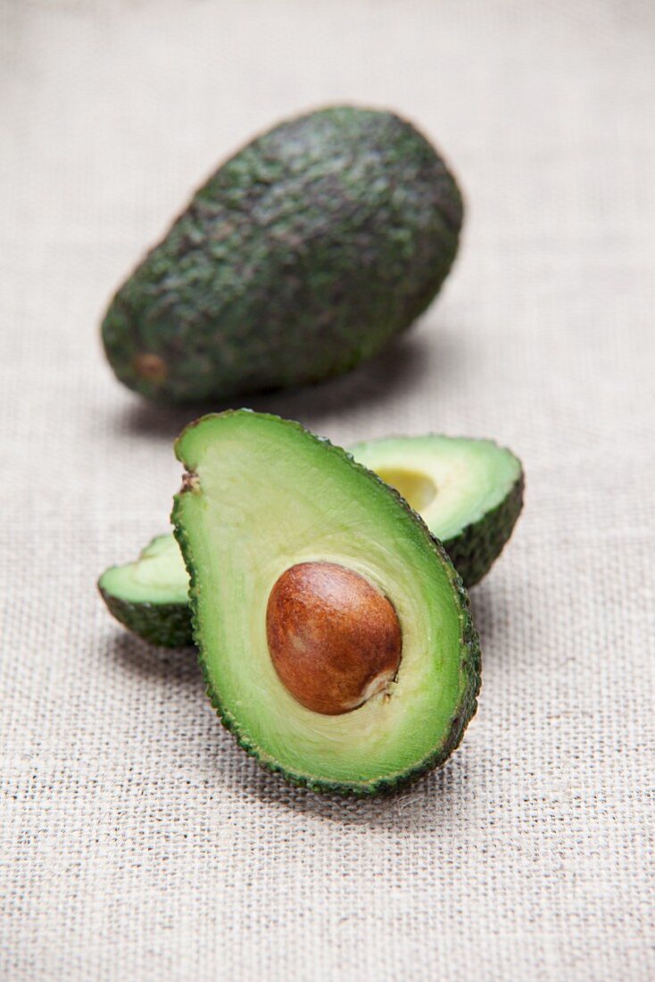 Avocados, whole and halved, on a fabric surface