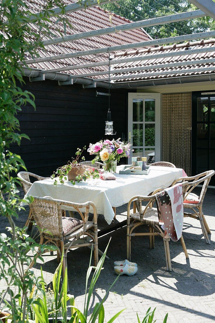 Blumenstrauss auf Tisch mit weisser Tischdecke unter Pergola einer sonnenbeschienenen Terrasse