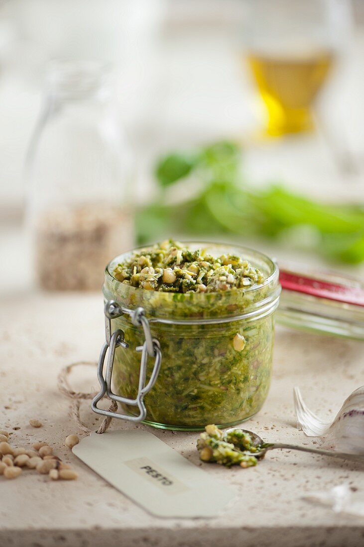 An open jar of fresh basil pesto surrounded by ingredients