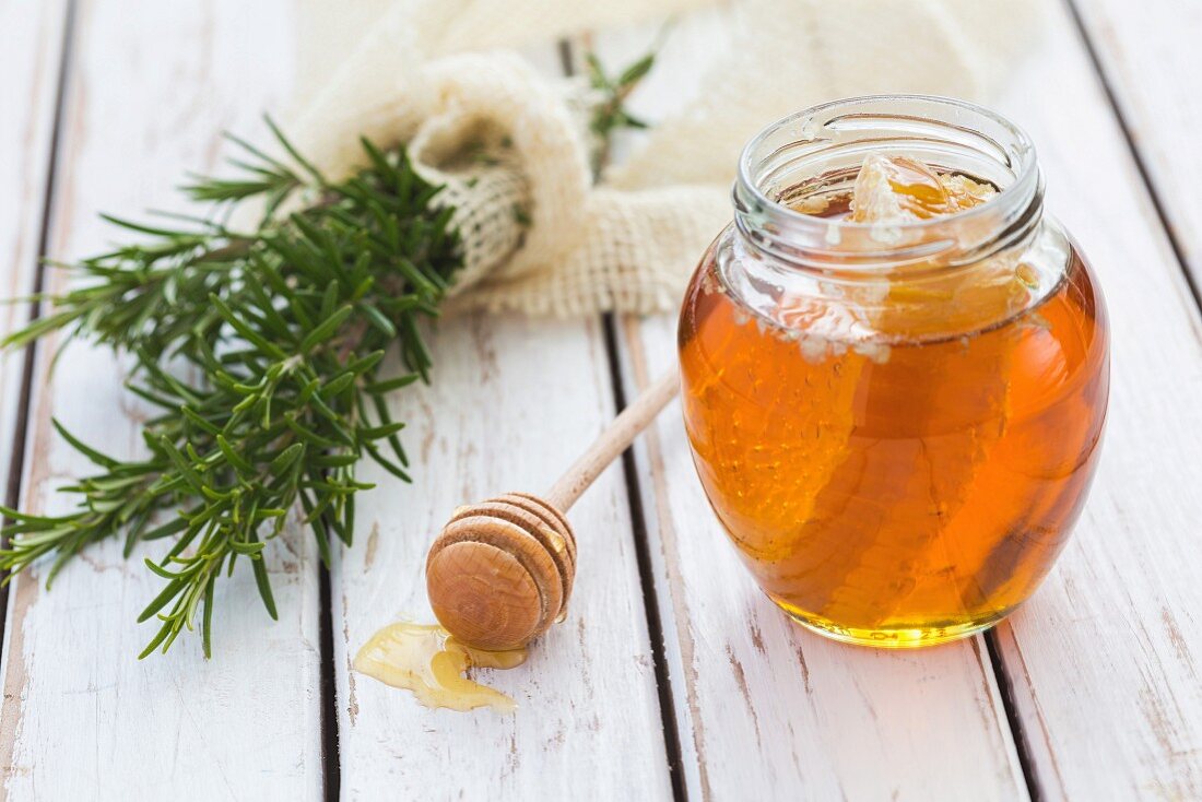 Honig mit Wabe im Glas, daneben frischer Rosmarin