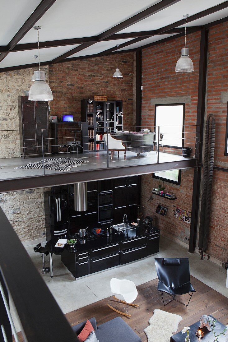 View from gallery down into loft interior with classic seating and open-plan black designer kitchen