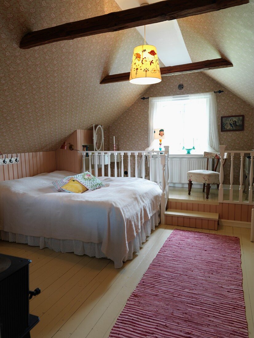 Attic bedroom; double bed with white bedspread in front of raised platform with white wooden balustrade