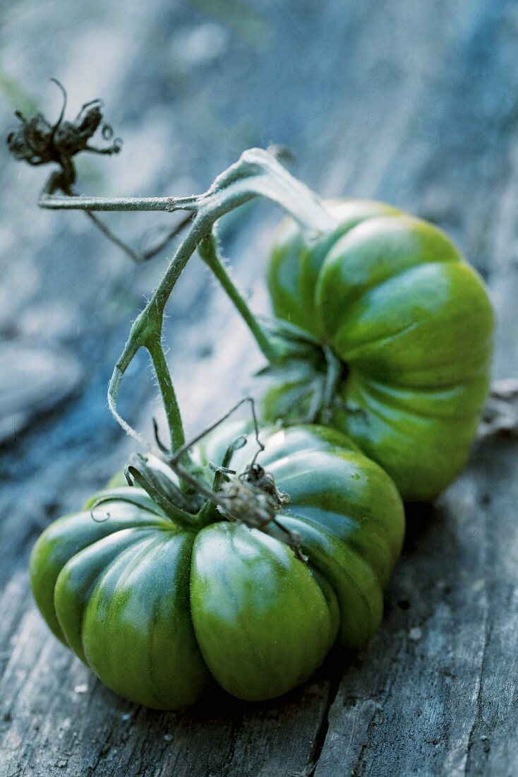 Two large, green beefsteak tomatoes on a wooden surface