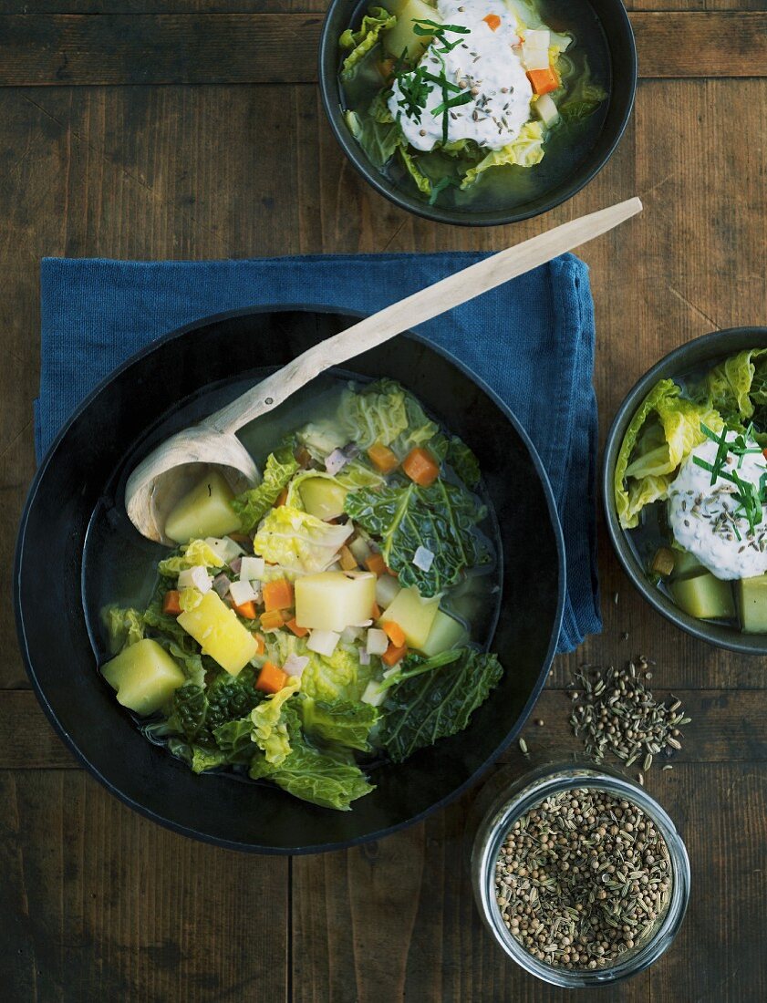 Savoy cabbage stew with sour cream flavoured with bread seasoning in a dark bowl with a wooden spoon